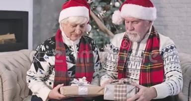 高加索人和积极的女人坐在沙发上拿着圣诞<strong>礼</strong>物。 丈夫看着他可爱的